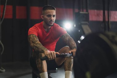 Dövmeli yakışıklı adam spor salonunda egzersiz yapıyor.