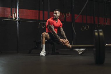 Erkek sporcu spor salonunda halterle dinleniyor.