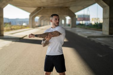 Dövmeleri olan, kameraya poz veren ve gülümseyen yakışıklı genç sakallı adam.