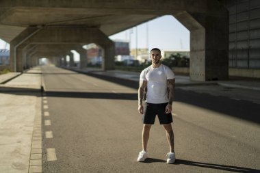 Genç erkek koşucu beyaz gömlekli ve siyah şortlu yolda koşuyor.