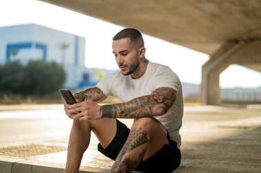 Dövmeli genç adam dışarıda dinlenirken akıllı telefon kullanıyor..