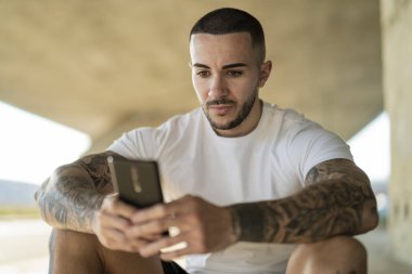 Akıllı telefonu olan genç yakışıklı adam merdivenlerde oturuyor..