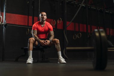 Genç kaslı adam spor salonunda oturuyor.