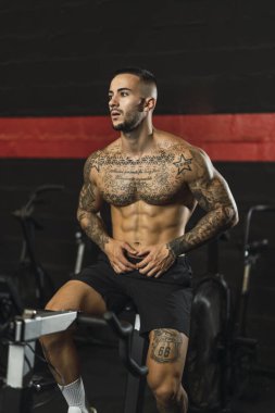 Dövmeli kaslı adam spor salonunda egzersiz yapıyor.