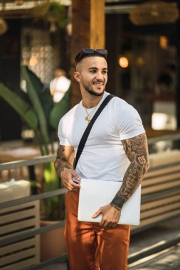 Sırt çantası ve dizüstü bilgisayarı olan gülümseyen genç adamın portresi.