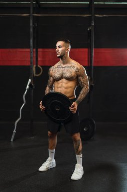 Spor salonunda çan çalan kaslı bir adam ağırlık egzersizi yapıyor.