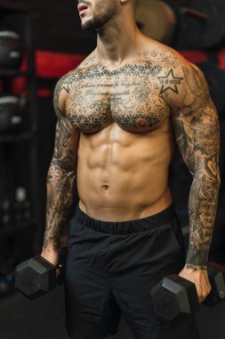 Spor salonunda dövmeli kaslı bir adam.