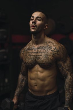 Modern spor salonunda poz veren dövmeleri olan genç ve yakışıklı bir adam.