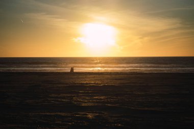 Gün batımında sahilde yürüyen bir adamın silüeti.