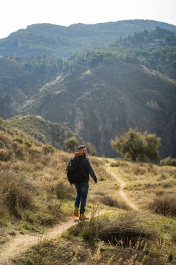 Sırt çantalı genç adam dağlarda ormanda yürüyüş yapıyor..