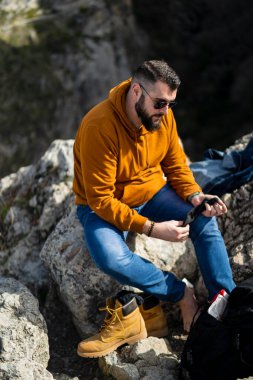 Genç sakallı adam kayalık bir uçurumun kenarında oturuyor..