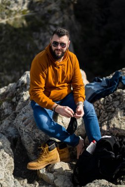 Güneş gözlüklü genç adam dağda oturuyor.