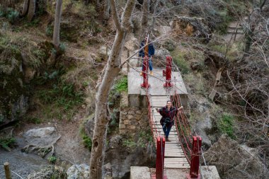 Dağ nehrinin arkasında sırt çantalı siyah elbiseli bir adam var.