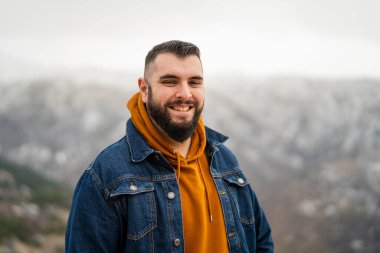 Gülümseyen, sakallı genç bir adamın portresi sıradan giysiler içinde karlı dağların arkasında dikiliyor. Adam gülümsüyor..