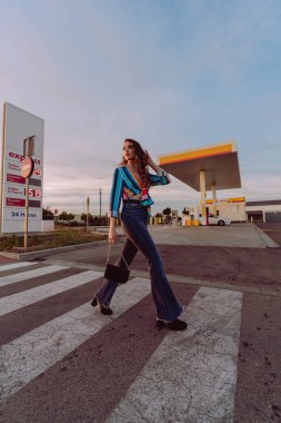 Uzun saçlı, kırmızı elbiseli genç bir kadın yolun ortasında yürüyor.