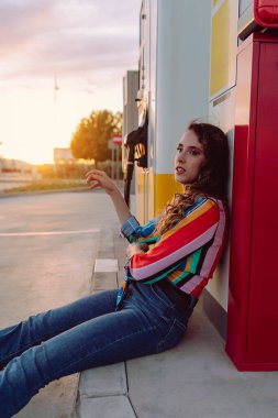 Kırmızı ceketli bir kadın eski bir arabanın önünde bavulun üzerine oturur.