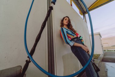 Güzel genç bir kadın garajda poz veriyor, korkuluklara yaslanıyor.