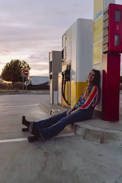 Arkasında benzin istasyonu olan genç bir kadın.
