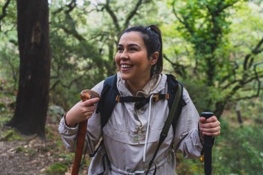 Sırt çantasıyla yürüyen ve gündüz vakti ormanda yürüyüş yapan gülümseyen bir kadın yürüyüşçü.