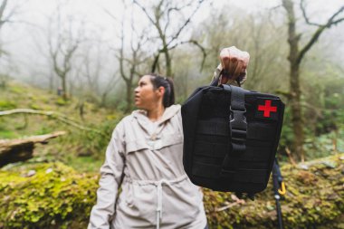 Kadın gönüllü koruyucu giysiler içinde sırt çantalı kırsal bölgedeki nehrin yakınındaki ormanda duruyor.
