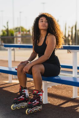 Kaykayın üzerinde oturan afro saçlı genç bir kadın.