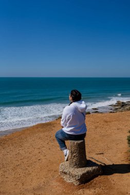Bir adam kayaya oturur ve denize bakar.