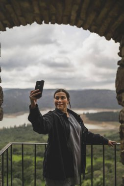 Kafasında sırt çantası ve elinde telefonu olan siyah ceketli genç bir kadın.