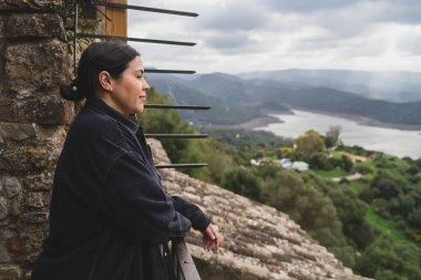 Dağlık bir bölgede, beyaz gömlekli, sırt çantalı bir kadın yürüyüşçünün dikey görüntüsü.