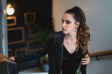 Siyah takım elbiseli, uzun siyah kıvırcık saçlı, beyaz ceketli genç bir kadın.