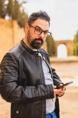 Ceketli bir adam kollarında ve kameraya bakıyor..