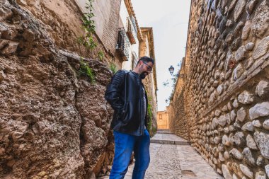 Şık ceketli yakışıklı genç adam antik bir şehrin sokaklarında yürüyor.