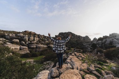 Sırt çantalı ve elleri dağın tepesinde duran genç bir adam..