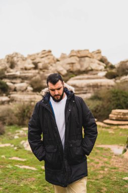 Beyaz gömlekli, sırt çantalı ve sakallı bir adam dağların arka planında bir kayanın üzerinde. yüksek kaliteli fotoğraf