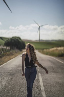 Kırsal yolun ortasındaki bir tarlada uzun kıvırcık saçlı güzel bir kadın. yüksek kaliteli fotoğraf