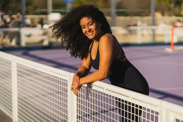 Sahada duran kıvırcık saçlı, gülümseyen genç kadının portresi.