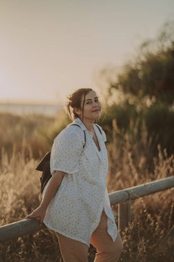 Gün batımında yolda yürüyen, sırt çantalı bir kadın..