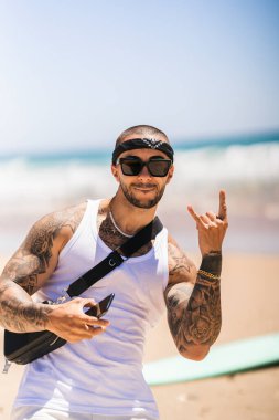 Güneş gözlüklü bir adam sırtında sırt çantasıyla poz veriyor ve baş parmağını gösteriyor.