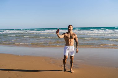 Siyah mayolu genç adam sahilde akıllı telefonuyla selfie çekiyor. yüksek kaliteli fotoğraf