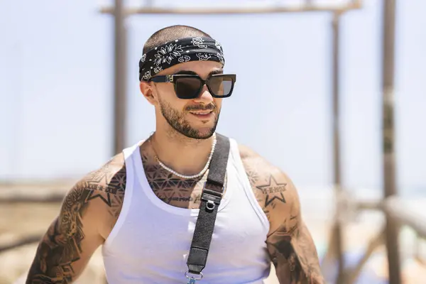 Kumsalda güneş gözlüğü takan dövmeli yakışıklı bir adam portresi.