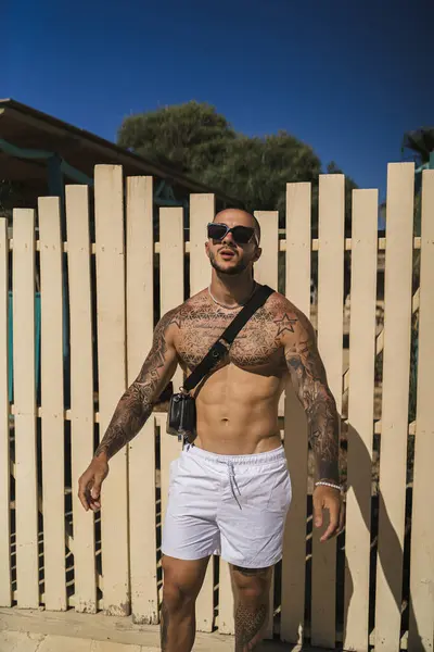 Parkta duran, güneş gözlüklü, kaslı bir gencin portresi.