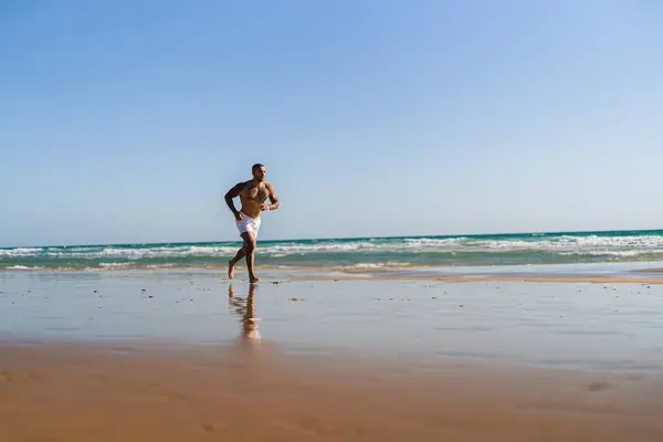 Siyah mayo giymiş Afro-Amerikan bir adam elleri kollarında denizde yürüyor..