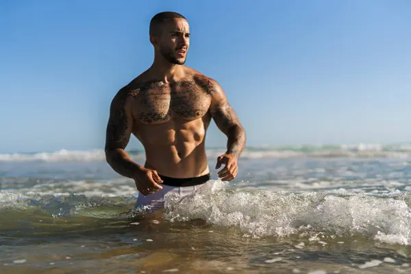 Güneşli bir günde denizde sörf tahtası olan üstsüz kaslı bir erkek.