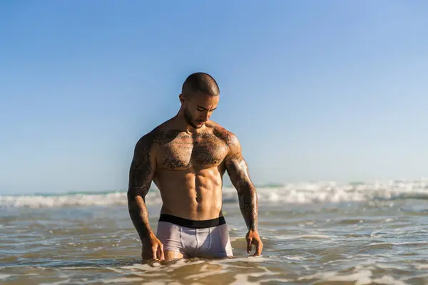 Deniz kıyısında elinde dövmesi olan kaslı bir adam.