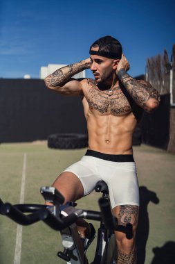 Kafasında dövme olan genç bir adam bisiklette oturuyor.