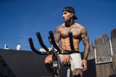 Güneşli bir günde dövmeli, bisikletli yakışıklı bir genç adam.