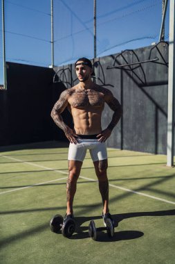 Çocuk parkında duran dövmeli ve gövdeli genç bir erkek sporcu.