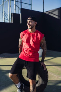 Şapkalı ve tişörtlü, toplu fit bir adamın portresi.