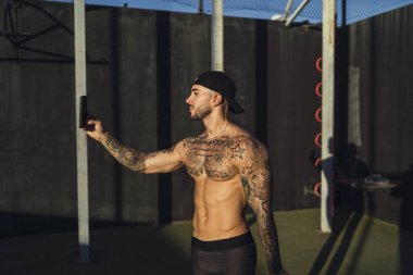 Dövmeleri olan genç bir sporcu sokakta egzersiz yapıyor.