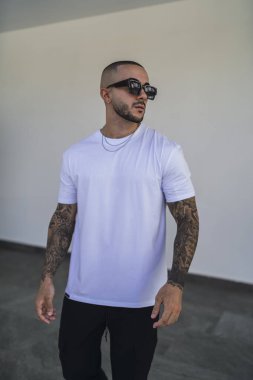 Sokakta beyaz tişörtlü ve dövmeli genç bir adam.