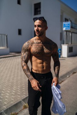 Açık havada duran dövmeleri olan yakışıklı, üstsüz genç bir adamın portresi..